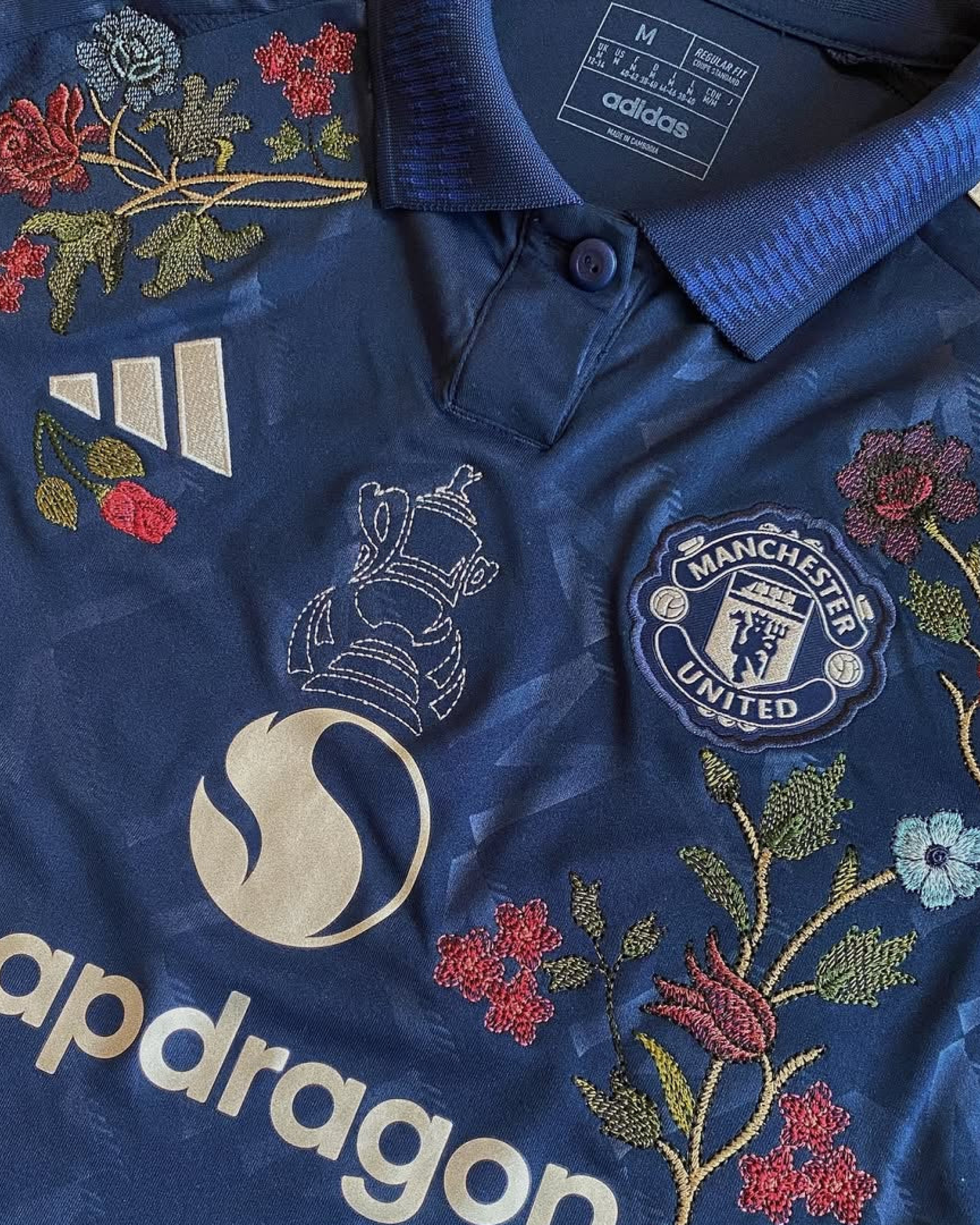 Close-Up Detail Of The Manchester United Embroidered Jersey Highlighting The Polo Collar, And Vibrant Roses.